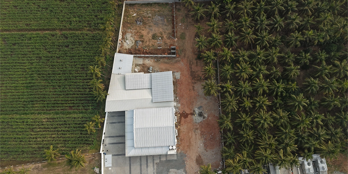 An event hall building surrounded by green fields coconut trees and open land showing overall layout
